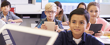 Image of grade-school children in a classroom sitting at their desks and holding computer tablets.