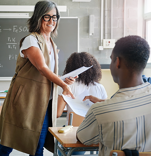 a teacher passing out papers to students in classroom