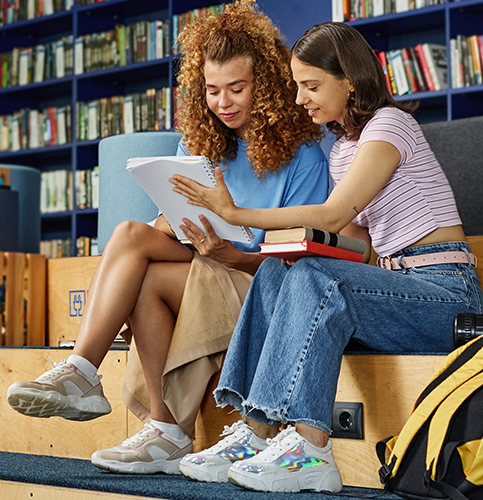 two students reading together while sitting on a bench in a school library