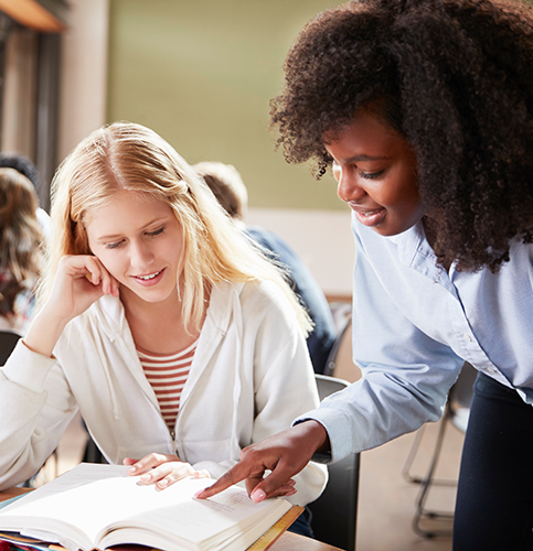 teacher and student looking at a book in a classroom
