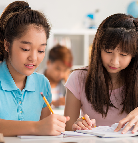 Image shows two girls writing in a notebook in class.