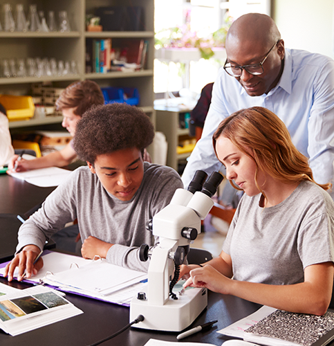 a teacher and two students in classroom at a desk doing science work with a microscope 