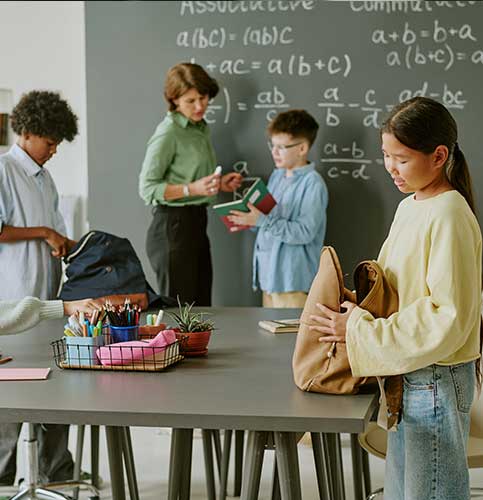 Image shows a female teacher reviewing homework at a desk.