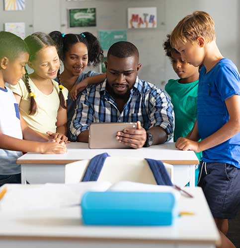 Image shows a female teacher reviewing homework at a desk.