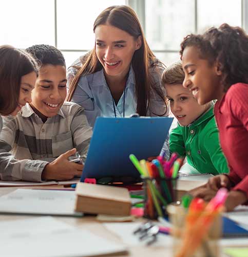Image shows a male teacher helping an elementary school age student working on a tablet.